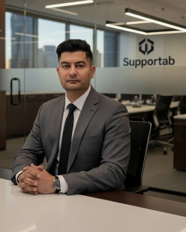 Ashish Malhotra, founder of Supportab, in a grey suit seated at a conference table in an office.